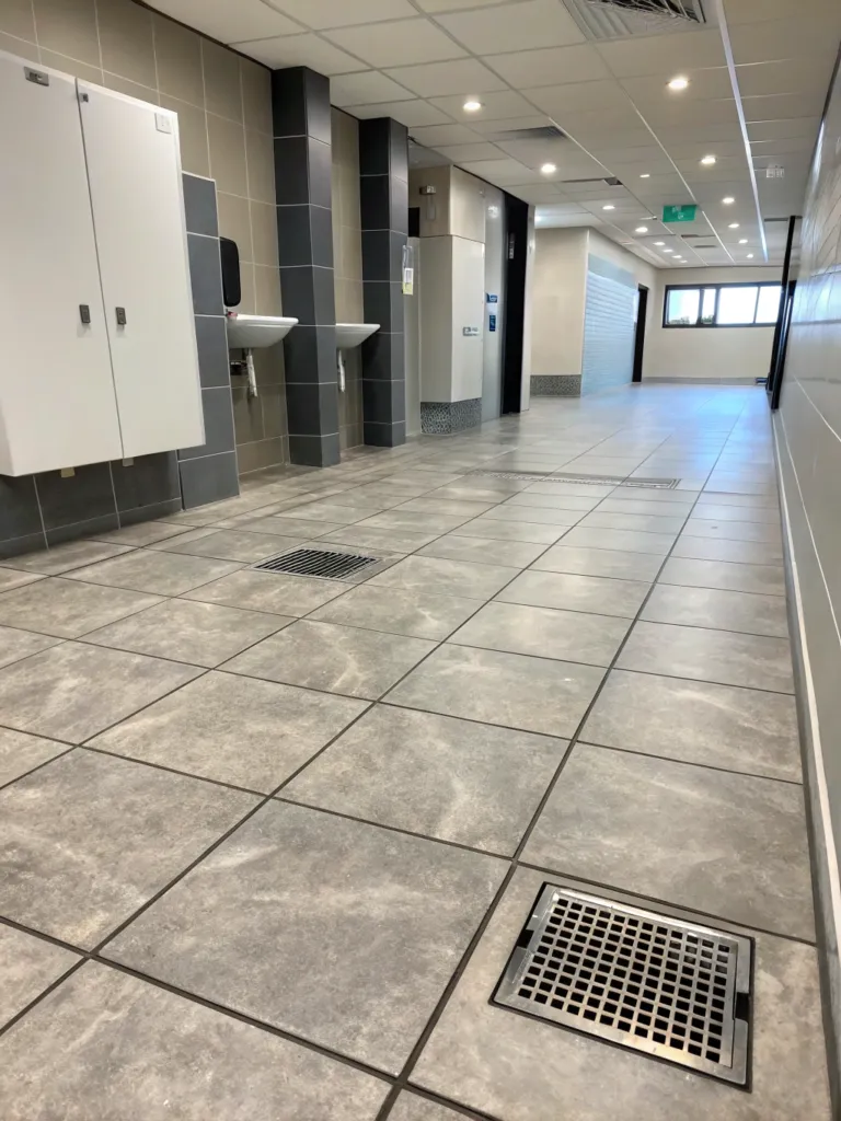 Large format floor tiling with floor drains in a commercial washroom corridor
